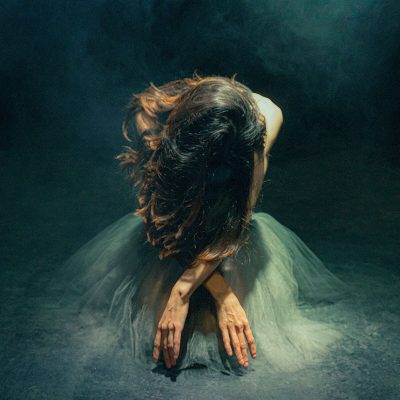 bailarina sentada en el piso con la cabeza baja rodeada de humo